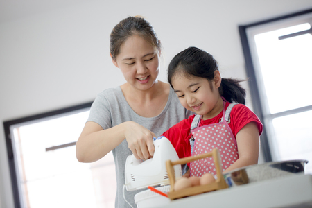 Little Asian cute chef cooking a bakery in kitchen with motherの写真素材