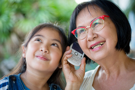 Little Asian girl calling mobile phone with her grandmotherの写真素材