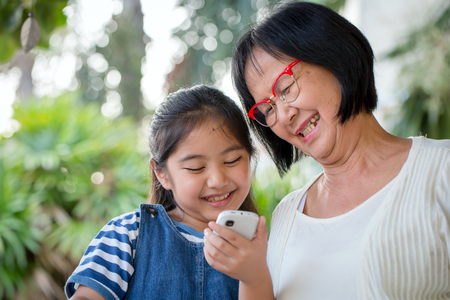 Little Asian girl calling mobile phone with her grandmotherの写真素材