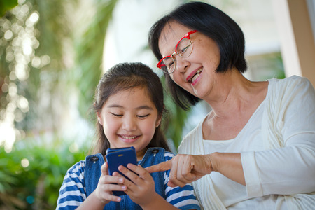 Little Asian girl touching smart phone with her grandmotherの写真素材