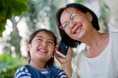 Little Asian girl calling smart phone with her grandmotherの写真素材