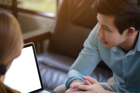 Young Asian businessman and woman meeting in coffee shop, using laptop for presentationの写真素材