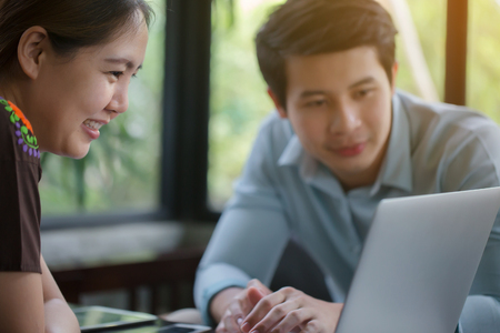 Young Asian businessman and woman meeting in coffee shop, using laptop for presentationの写真素材