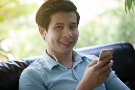 Young Asian man playing game online smart phone in cafeの写真素材