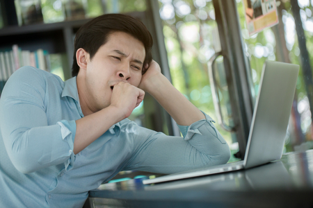 Sleepy young Asian worker with laptop computerの写真素材