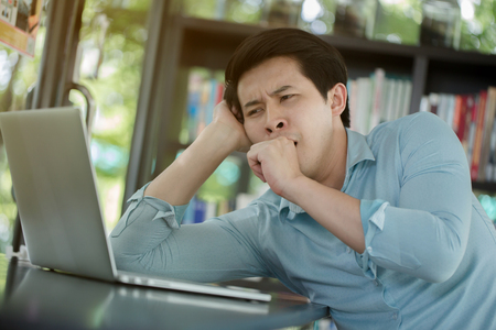 Sleepy young Asian worker with laptop computer, Hard workの写真素材