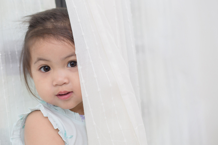 Asian girl playing hide and seek behind the curtainの写真素材