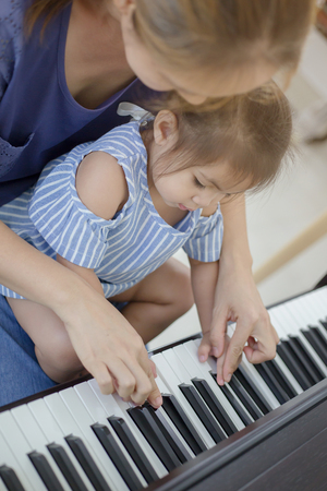 Happy little Asian girl playing piano with mother at homeの写真素材