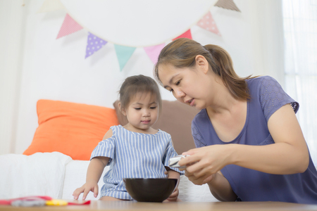 Happy Asian mother feeding delicious cornflake or her daughterの写真素材