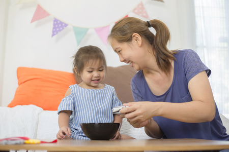 Happy Asian mother feeding delicious cornflake or her daughterの写真素材