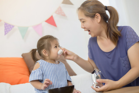 Happy Asian mother feeding delicious cornflake or her daughterの写真素材
