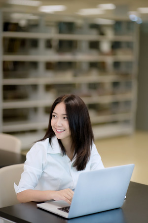 Portrait of a happy beautiful Asian young woman using laptop in officeの写真素材