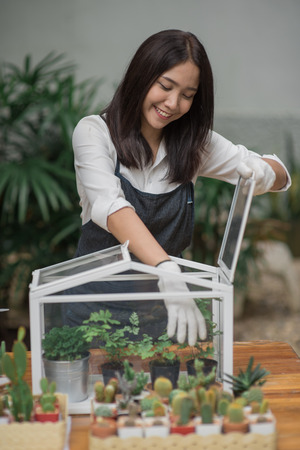 Happy young Asian woman putting plant to mini glass houseの写真素材