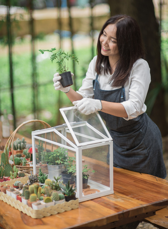 Happy young Asian woman putting plant to mini glass houseの写真素材