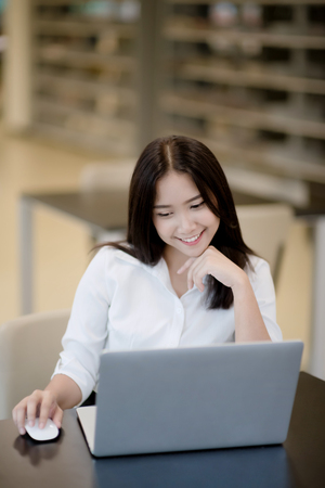 Portrait of a happy beautiful Asian young woman using laptop in officeの写真素材