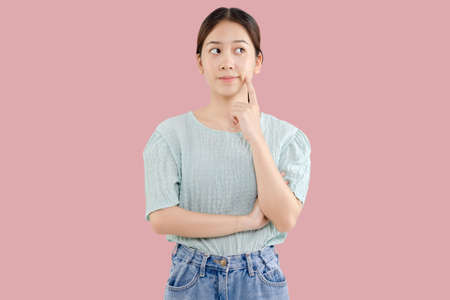 Beautiful young Asian girl thinking and looking upwards. The concept of content thinks about future isolated on pink background.の写真素材