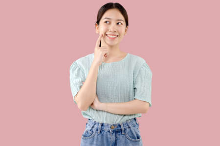 Beautiful young Asian girl thinking and looking upwards. The concept of content thinks about future isolated on pink background.の写真素材