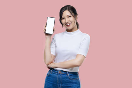 Happy young Asian woman feeling happiness and gesture showing mobile smartphone blank screen on isolated pink background.の写真素材
