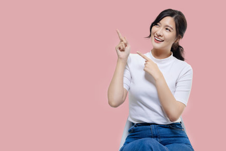 Happy young Asian woman feeling happiness and gesture pointing finger on isolated pink background with copy space.の写真素材