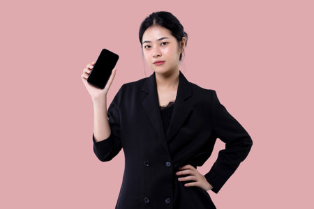 Young modern business asian woman holding smartphone mobile device and showing blank screen display isolated over pink background.の写真素材