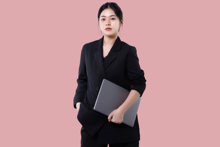 Young modern business asian woman holding laptop computer isolated over pink background.の写真素材