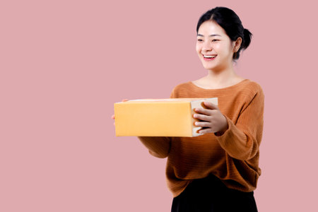 Happy Asian woman holding parcel box isolated over pink background.の写真素材