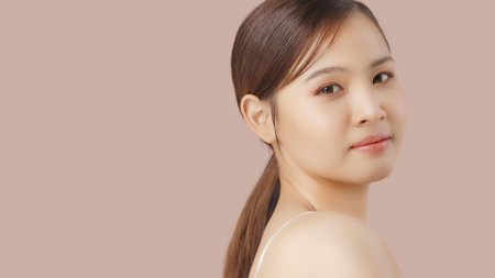 Close up portrait beauty shot of Beautiful Asian girl looking at camera isolated on brown background with copy space.の写真素材