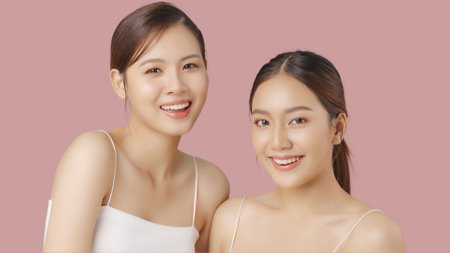 Close up portrait beauty shot of two young beautiful Asian girls looking at camera isolated on pink background.の写真素材