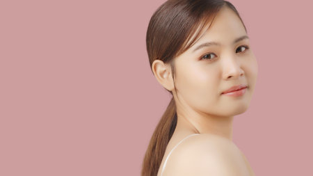 Close up portrait beauty shot of Beautiful Asian girl looking at camera isolated on pink background with copy space.の写真素材