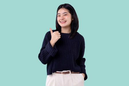 Cheerful young Asian woman showing thumbs up gesture isolated over blue backgroundの写真素材