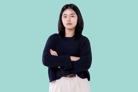 Portrait of young Asian woman standing with arms crossed isolated on blue backgroundの写真素材