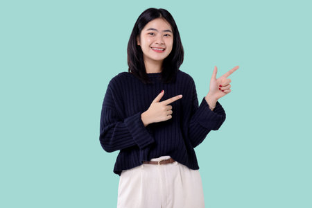 Portrait of smiling asian woman pointing fingers at copy space isolated on blue backgroundの写真素材