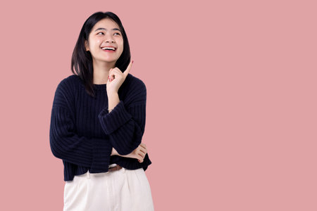 Happy young Asian woman feeling happiness and gesture pointing finger to the side isolated on pink background.の写真素材