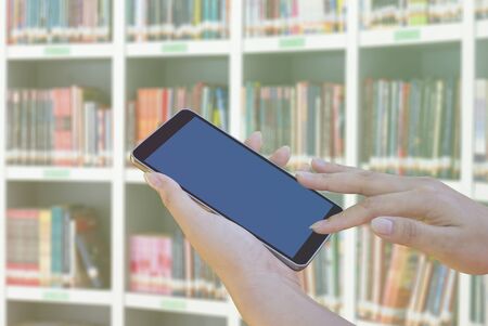 hands using mobile phone at book shelves in libraryの写真素材
