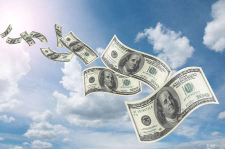 flying dollar bills in flocks in blue sky の写真素材