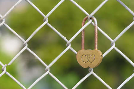 Closeup rusty heart shaped padlock locked on iron chain
