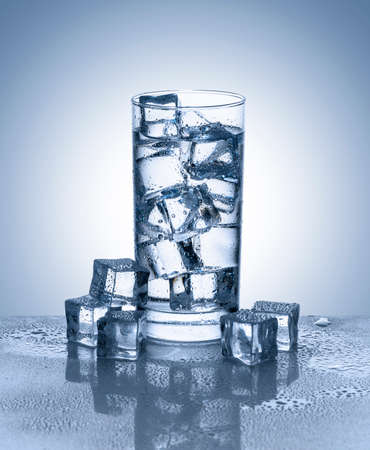 Glass of water with ice cubes on reflective surfaceの写真素材