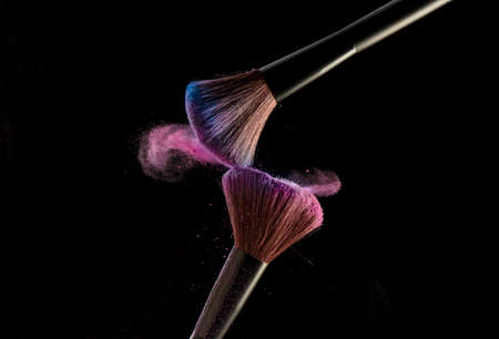 Make-up brushes with pink powder explosion on black backgroundの写真素材