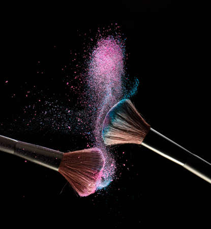 Make-up brushes with pink and blue powder explosion on black backgroundの写真素材