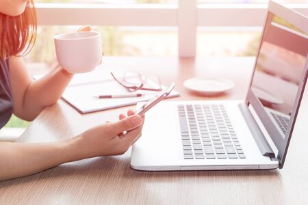 Close Up of woman hands using mobile phone and laptop computer business with blank copy space screen for your business advertising text message or content business in the morning light.の写真素材