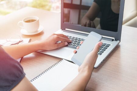 Close Up of woman hands using mobile phone and laptop computer business with blank copy space screen for your business advertising text message or content business in the morning light.の写真素材