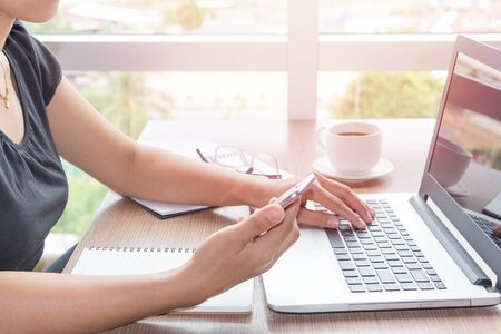 Close Up of woman hands using mobile phone and laptop computer business with blank copy space screen for your business advertising text message or content business in the morning light.の写真素材