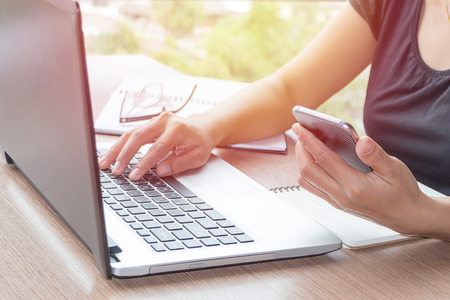 Close Up of woman hands using mobile phone and laptop computer business with blank copy space screen for your business advertising text message or content business in the morning light.の写真素材