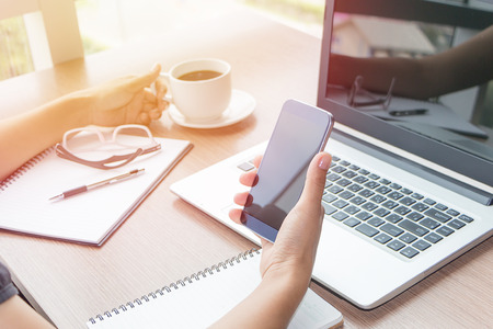 Close Up of woman hands using mobile phone and laptop computer business with blank copy space screen for your business advertising text message or content business in the morning light.の写真素材