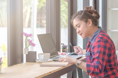 Close Up of woman hands using mobile phone and laptop computer with blank copy space screen for your advertising text message or content business at a coffee shop with a document.の写真素材