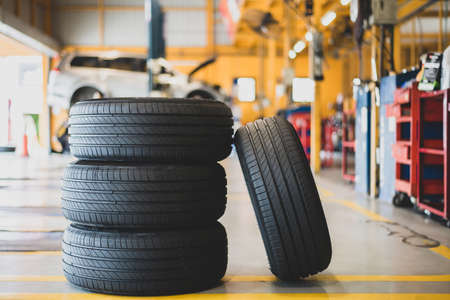 Four new tires lie on the floor inside the garage and blur cars and repair equipment in the background.の写真素材