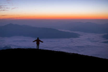 Silhouette of young traveler standing alone on top of the mountain and watched beautiful view of foggy landscape and sunrise in national park. It is a beautiful natural phenomenon in the morning.の写真素材