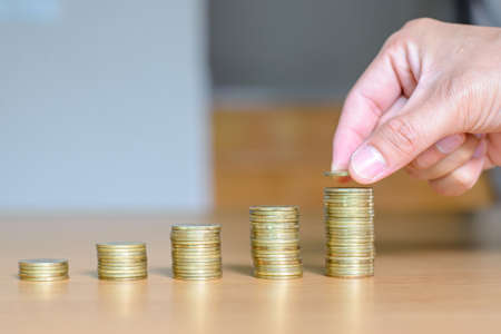 Saving money concept. Male hand putting money coin stack for the future growing business, education and retirement. He felt that saving money made his life safe.の写真素材