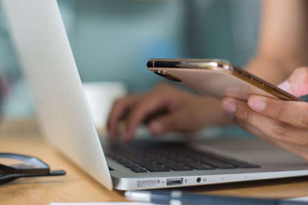 Female hand holding smart phone on office deck with laptop, coffee to pay for items through an online payment system. Online shopping is the best option to reduce the spread of the coronavirus.の写真素材