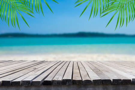 Empty wooden table in front of blurred background of the sea, sand, mountain, coconut palm, blue sky among bright sunlight on a clear day. Can be used for display or montage for show your products.の写真素材